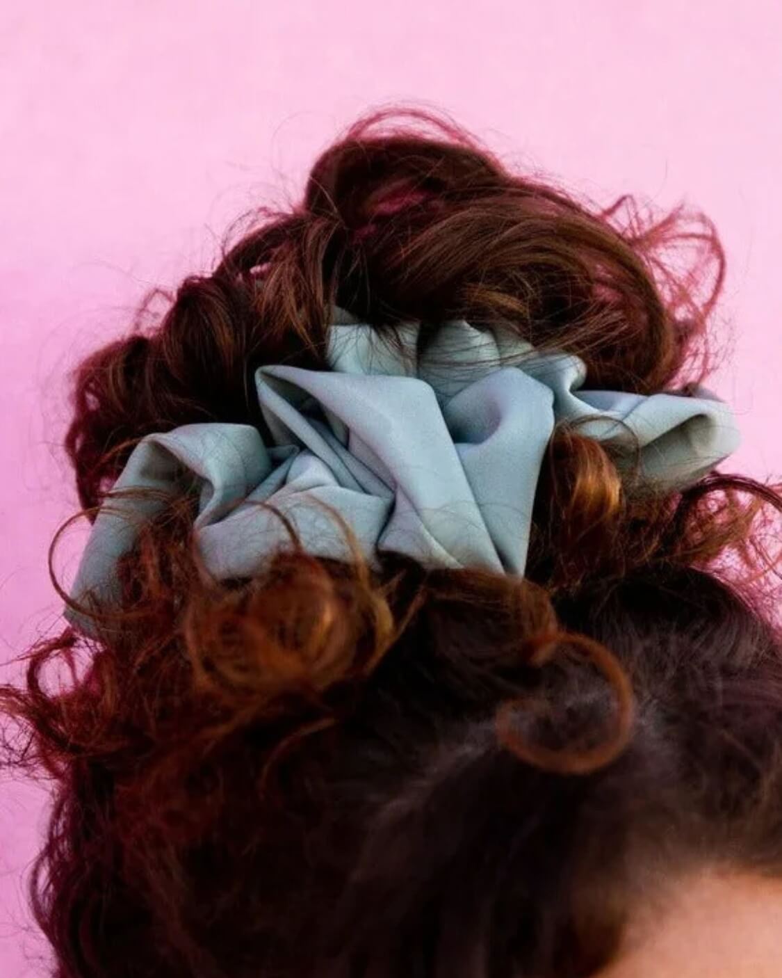 Close-up of the Eucalyptus Jumbo Scrunchie on a pink background showing the luxe sateen fabric and light blue green matte finish.
