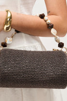 Close-up of model wearing the chocolate Rachel Straw Clutch highlighting the textured woven exterior, faceted bead details, polished hardware, and zip-top closure.