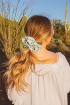 Rear view of model styling the Eucalyptus Jumbo Scrunchie highlighting the soft sateen material and eucalyptus blue green tone in a voluminous hairstyle.