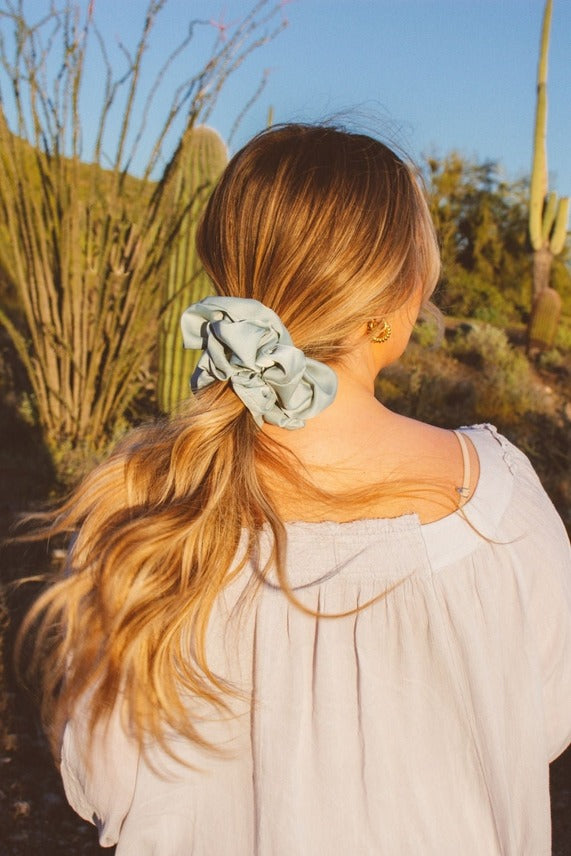 Rear view of model styling the Eucalyptus Jumbo Scrunchie highlighting the soft sateen material and eucalyptus blue green tone in a voluminous hairstyle.