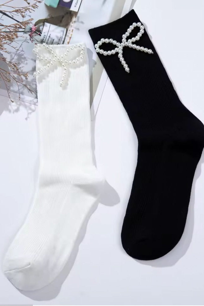 Black and white ribbed crew socks featuring delicate pearl bow embellishments, styled flat lay on a light background.