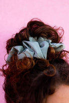Close-up of the Eucalyptus Jumbo Scrunchie on a pink background showing the luxe sateen fabric and light blue green matte finish.