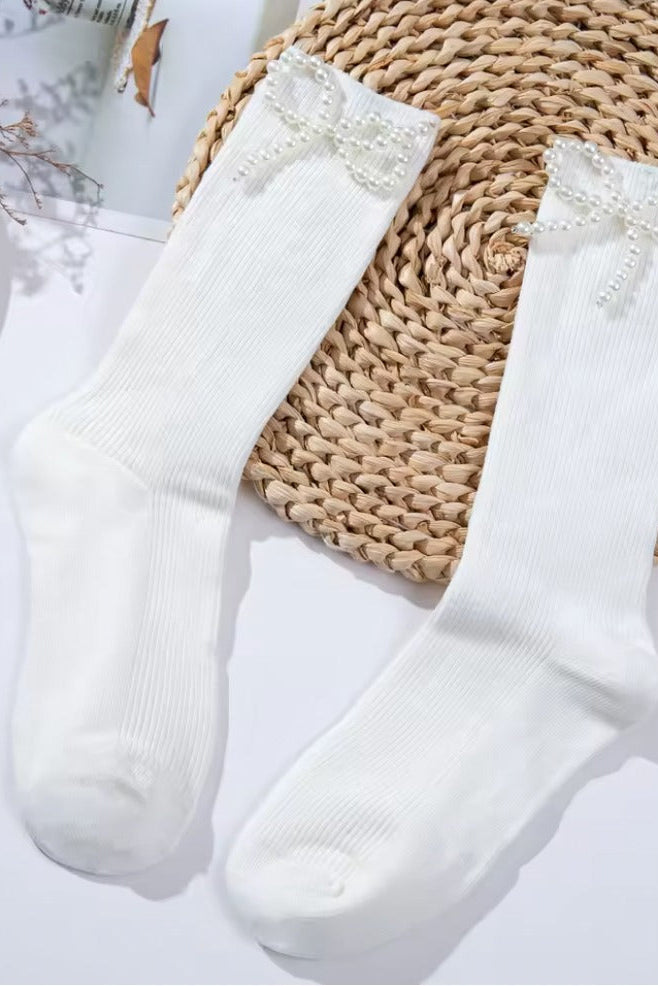 White ribbed crew socks featuring delicate pearl bow embellishments, styled flat lay on a light background.