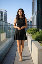 Slow Dancing Mini Dress featuring a sleeveless fitted bodice with flared skirt, styled on a rooftop walkway with city surroundings, highlighting the flattering fit and effortless evening wear.