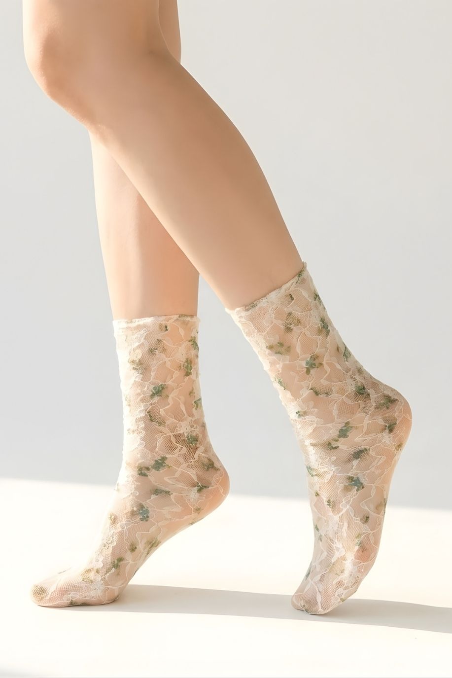 Floral mesh sheer socks in a muted green floral pattern, styled on both feet in a clean studio setting to highlight the soft mesh fabric and delicate lace details.