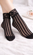 Black floral lace vertical stripe fishnet ankle socks worn with lace cuff detail, styled on feet against a soft neutral background.