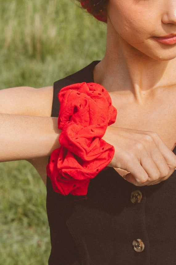 Close-up of the Red Eyelet Jumbo Scrunchie displaying the vibrant red eyelet fabric texture and stretchy jumbo silhouette.