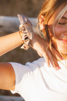 Close-up of the Chestnut Bow Scrunchie worn on the model’s wrist highlighting the creamy chestnut brown tone, bow design, and subtle shiny finish.