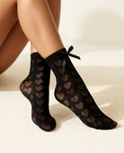 Black Heart-Shaped Lace Bow Socks on model, feet crossed on a cream floor