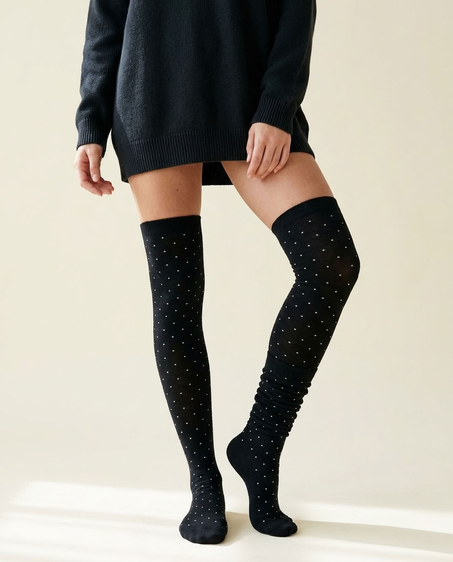 Long Polka Dot Socks in black with white polka dots, one pulled over the knee and one scrunched down the calf, worn with a black sweater dress.