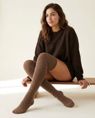 Long Polka Dot Socks in medium brown with cream polka dots, worn over the knee with a chocolate brown sweater, seated on a wooden bench.